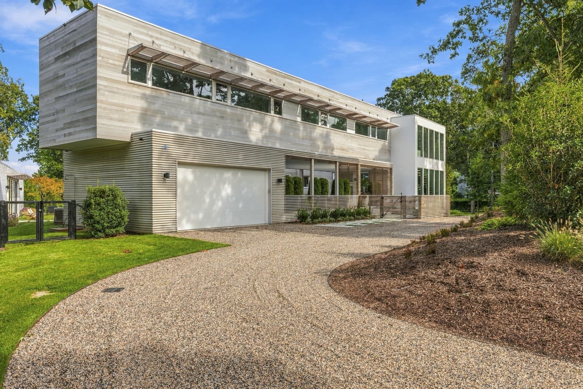 Modern two-story home with a long gravel driveway and mature trees
